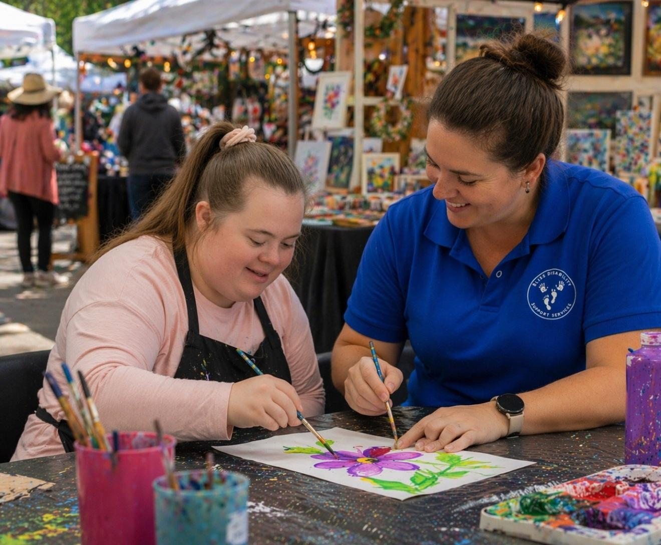 Young woman painting a flower with a support worker at an outdoor art market