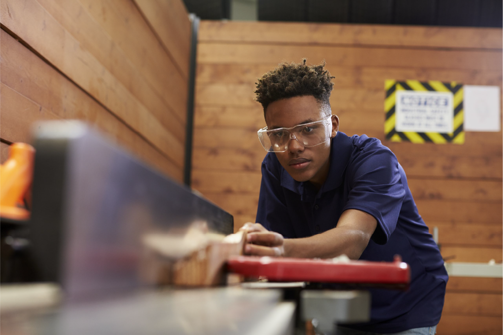Young man in safety glasses working at a bench in a woodwork shop