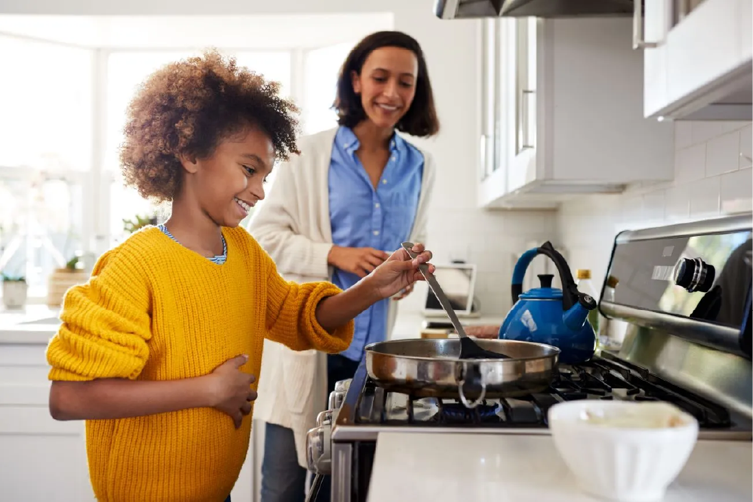 Young person cooking at the stove while a support worker stands alongside
