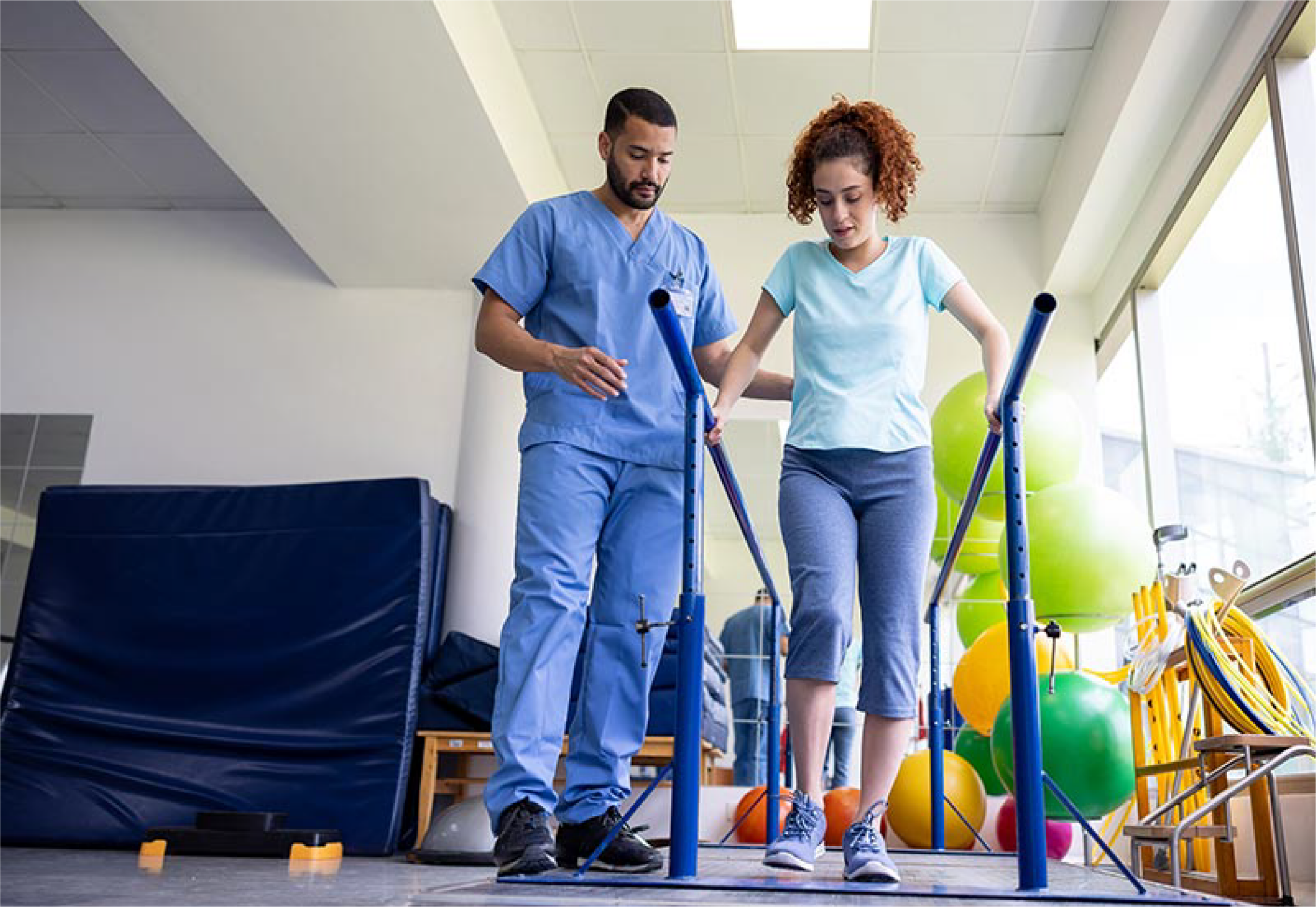 Young woman practicing walking between parallel bars with a therapist supporting her